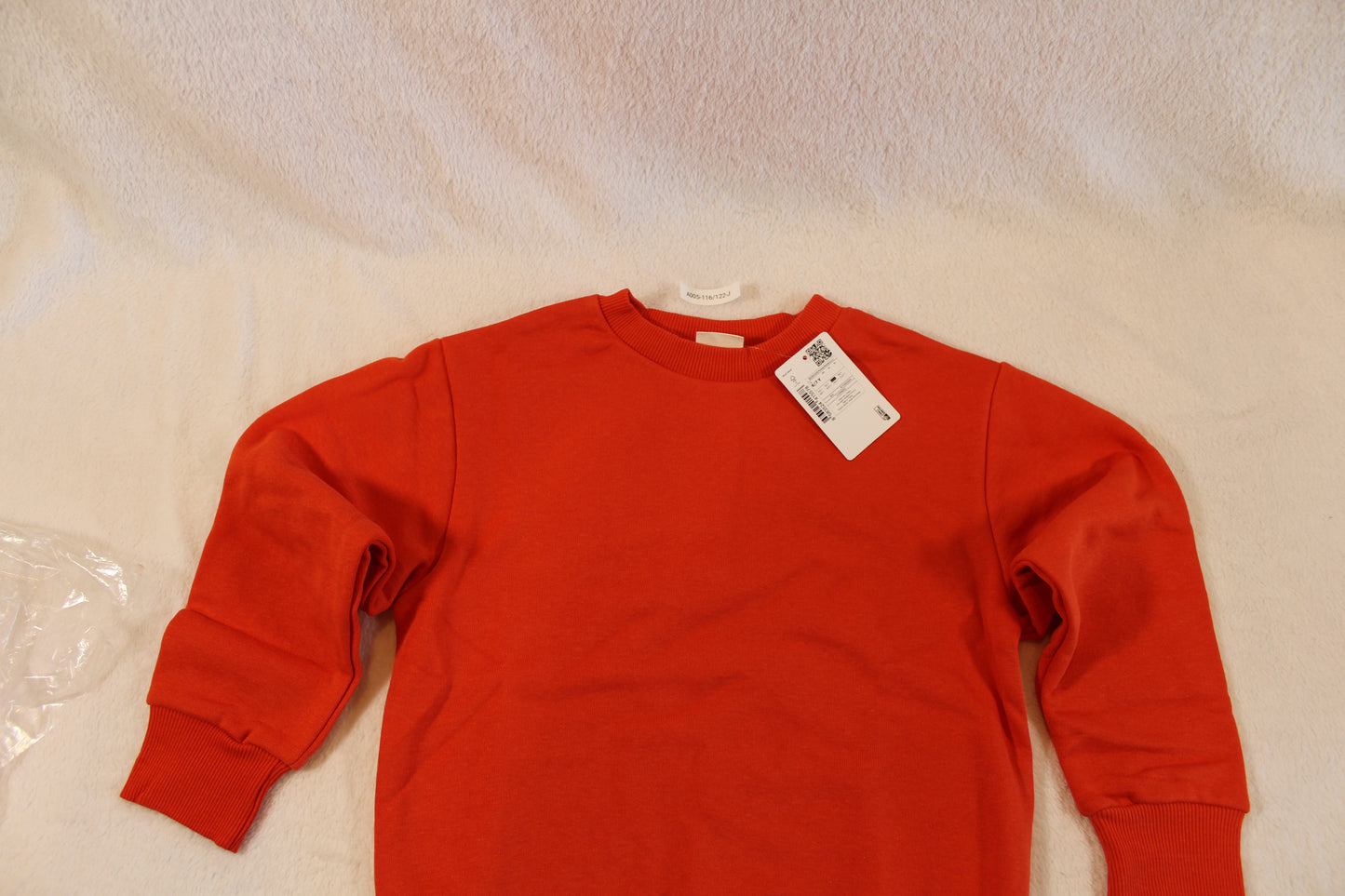 Red long-sleeve sweatshirt laid flat on a light surface with a visible white tag near the collar, showcasing the 116/122 Uni Pullover.