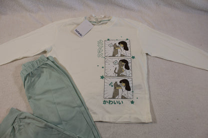 Light green pants and a white long-sleeve top featuring a cartoon girl and dog in comic panels with Japanese text, shown as part of Schlafanzug 110/116 set.