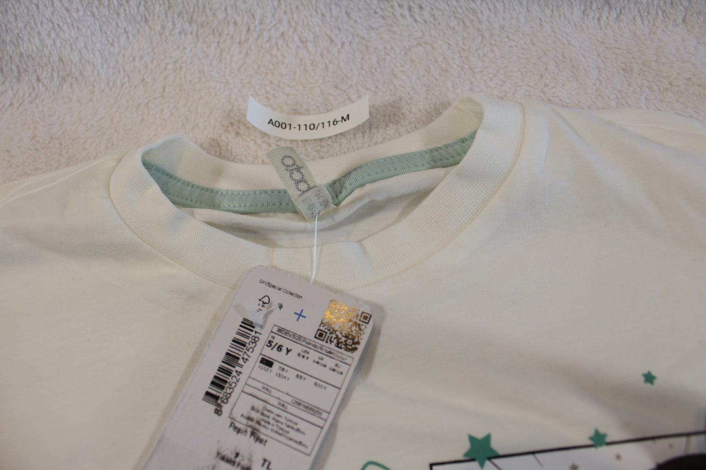 Close-up of a white children’s Schlafanzug 110/116 pajama top with a green trim inside the collar and a printed design featuring stars.