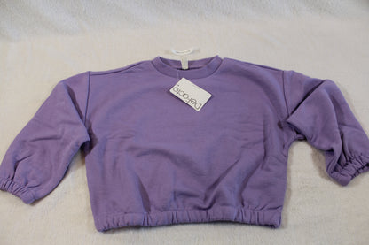 110/116 schöner Uni Pullover in soft purple fabric laid flat on a light surface with a tag attached, featuring long sleeves and elastic cuffs.