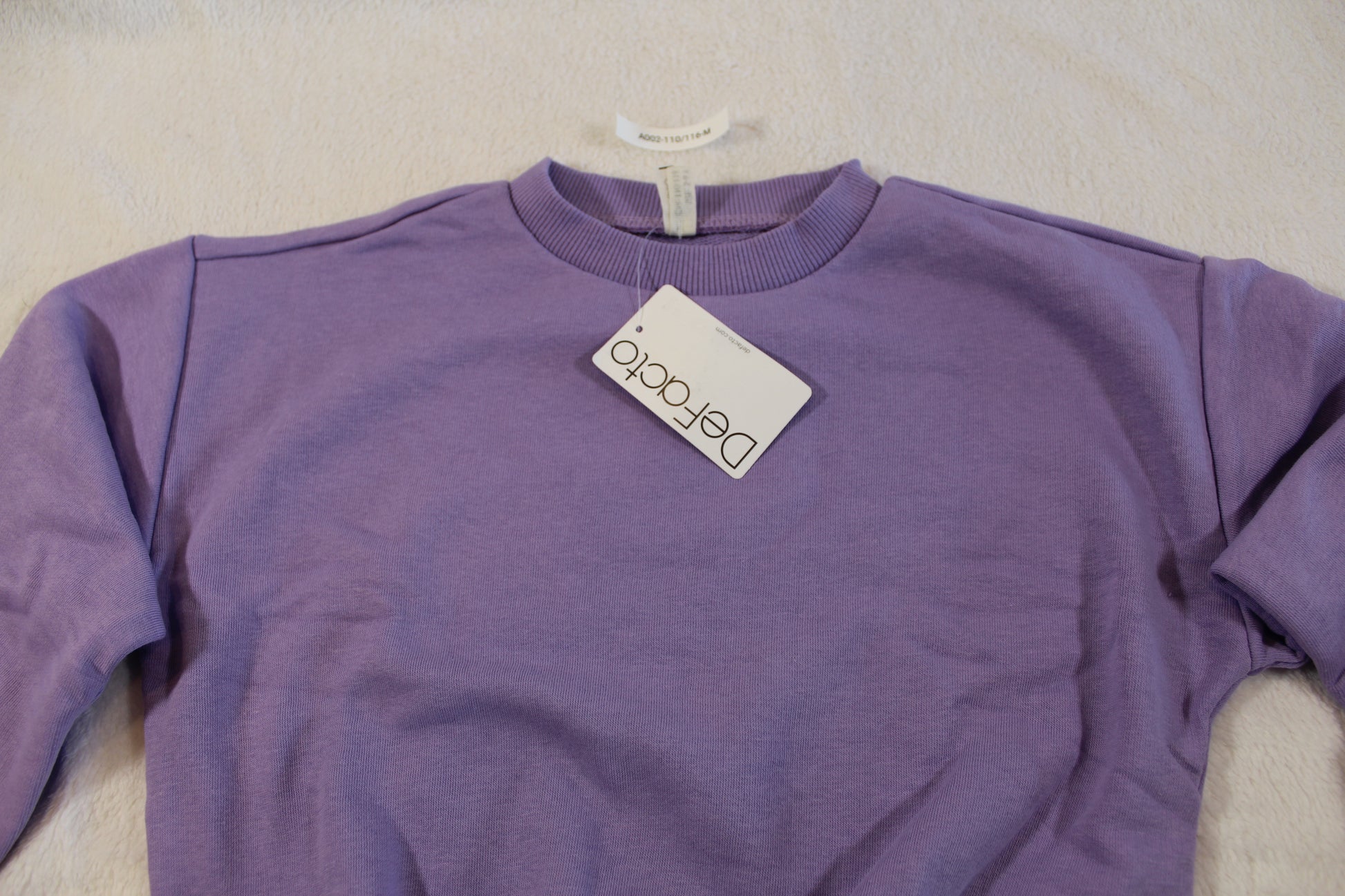 110/116 schöner Uni Pullover in a soft purple color, laid flat showing its simple, comfortable design with a round neckline and long sleeves.