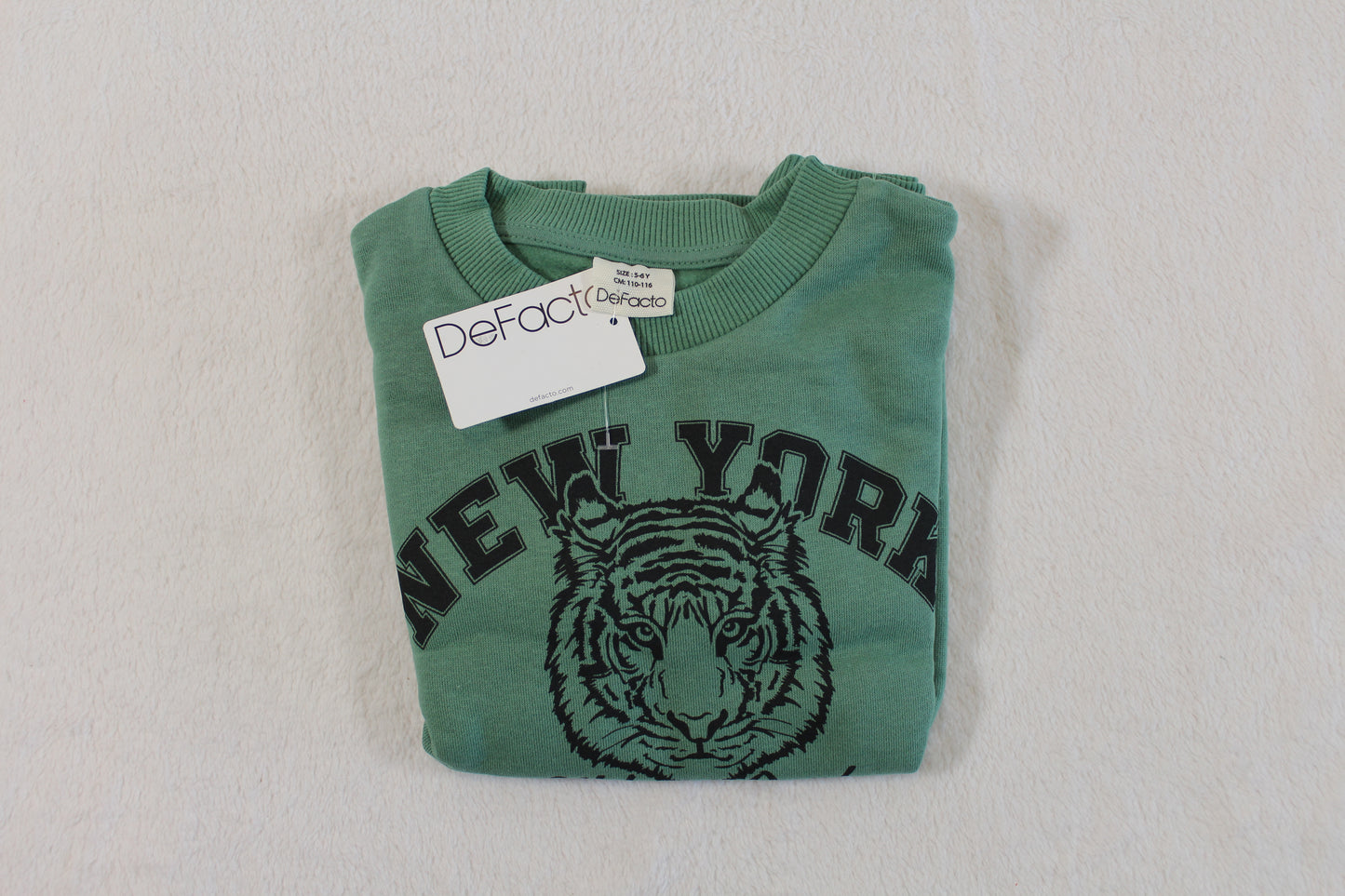 Folded green sweatshirt featuring a tiger face and "New York" text, labeled with the tag "110/116 Tiger Style" on a neutral background