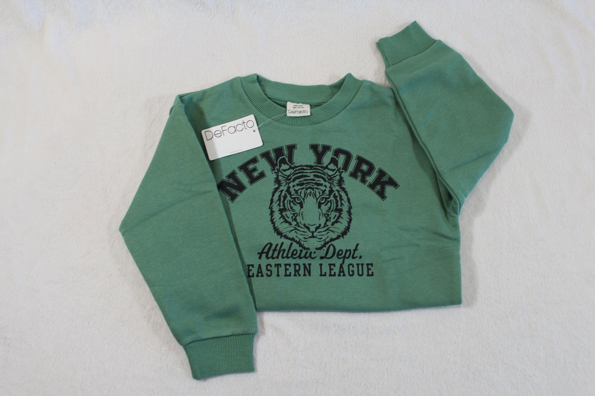 Folded green sweatshirt with tiger graphic and text "NEW YORK Athletic Dept. EASTERN LEAGUE," labeled "110/116 Tiger Style" displayed on a white surface.