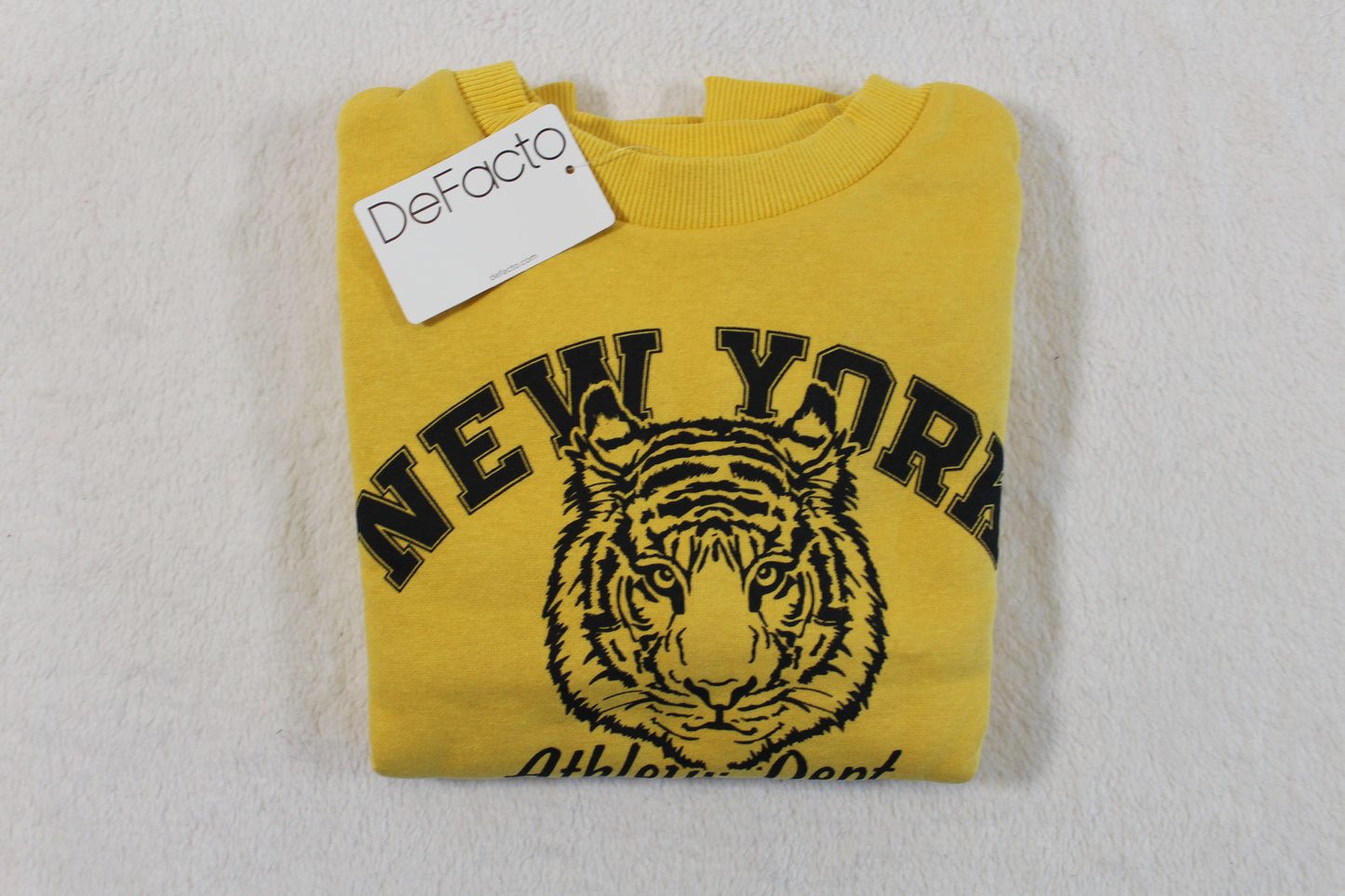 Folded yellow sweatshirt with black tiger graphic and "New York" text, featuring a DeFacto tag, 110/116 Tiger Style Pullover.