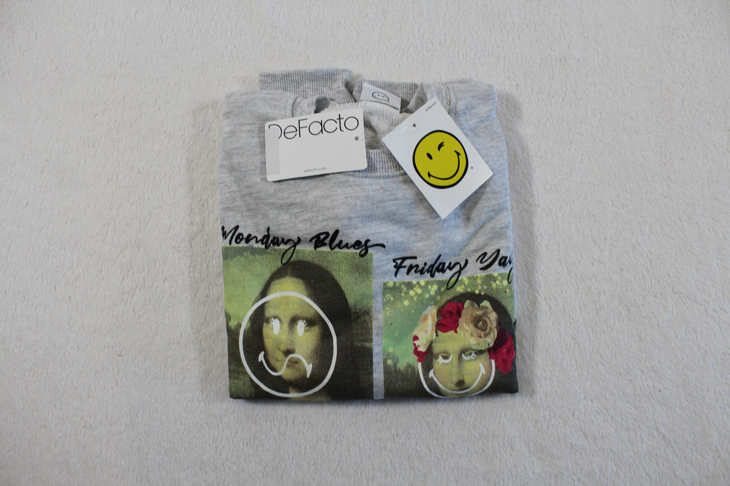 Folded grey pullover with artistic Mona Lisa prints and smiley face tags, featuring the "134/140 Monalisa Style Pullover" label.