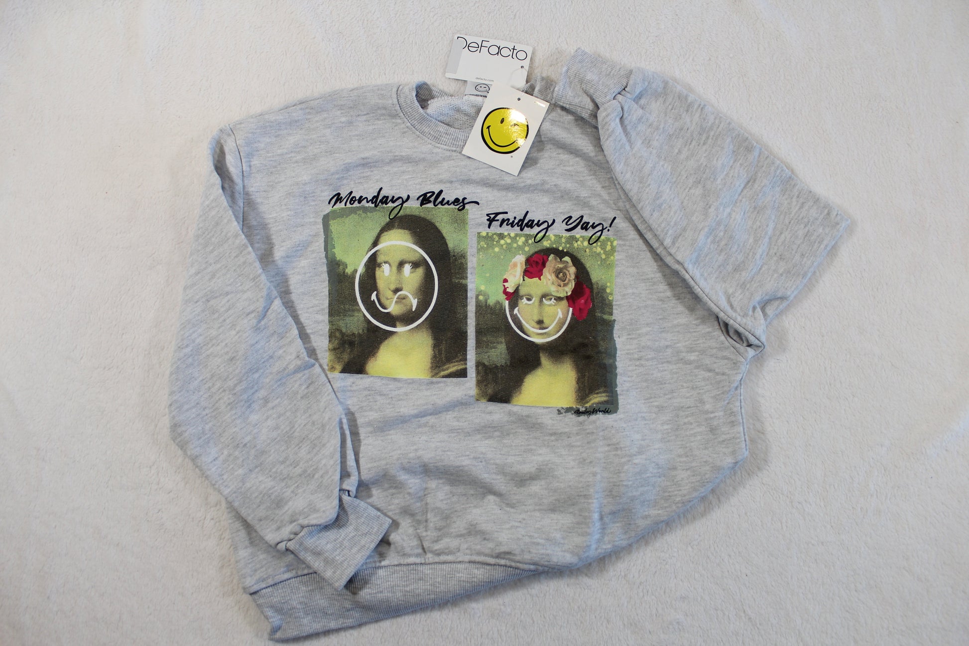 134/140 Monalisa Style Pullover with light gray fabric featuring playful prints of the Mona Lisa expressing "Monday Blues" and "Friday Yay" on the front.