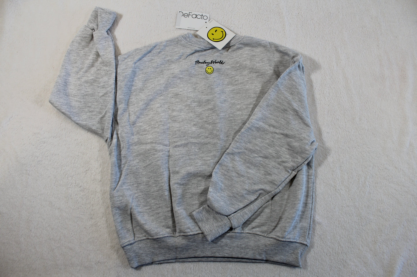 Light grey casual sweatshirt with long sleeves, a small yellow smiley face emblem on the chest, and the label visible on the collar, featuring the 134/140 Monalisa Style Pullover design.